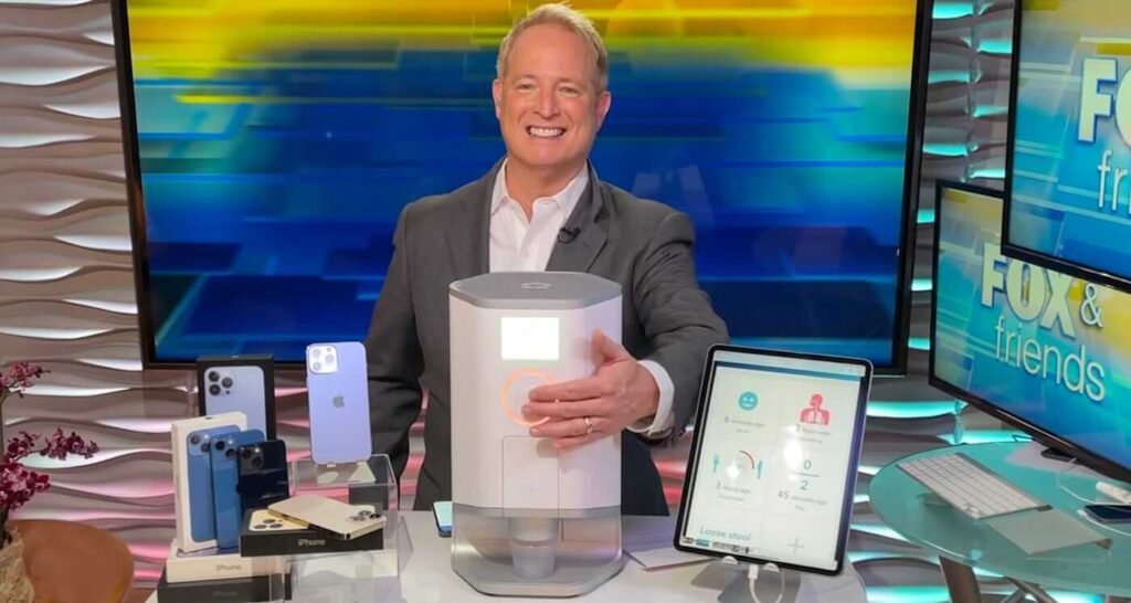 Kurt 'CyberGuy' Knutsson presenting various gadgets, including smartphones and a modern tech device, on a set with vibrant blue and yellow backgrounds, labeled 'FOX & Friends' on nearby screens.