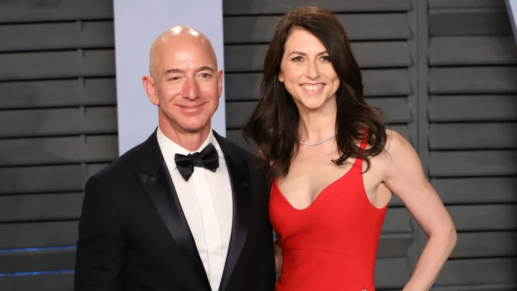 Jeff Bezos wearing a black tuxedo and bow tie, standing next to his ex-wife, MacKenzie Scott, who is dressed in a red gown, both smiling at a formal event.