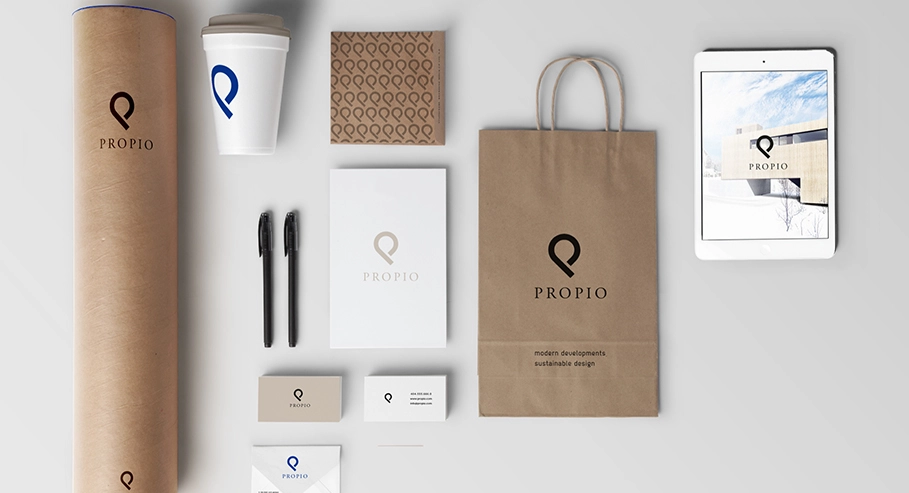 Brand identity mockup for ‘PROPIO’ featuring a paper cup, packaging materials, business cards, pens, a tablet displaying a map, and a shopping bag, all with the same logo and coordinated color scheme.